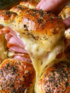 Une main soulève un slider montrant un étirement spectaculaire de fromage fondu (mini sandwichs jambon-fromage).