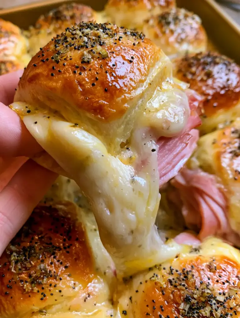 Vue de dessus d'un plat blanc rempli de mini sandwichs jambon-fromage avec glaçage brillant aux oignons et pavot.